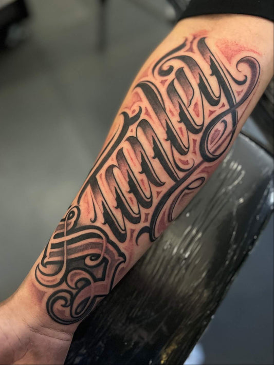 Tattoo on a person's arm with black and red ink, set against a blurred indoor background.